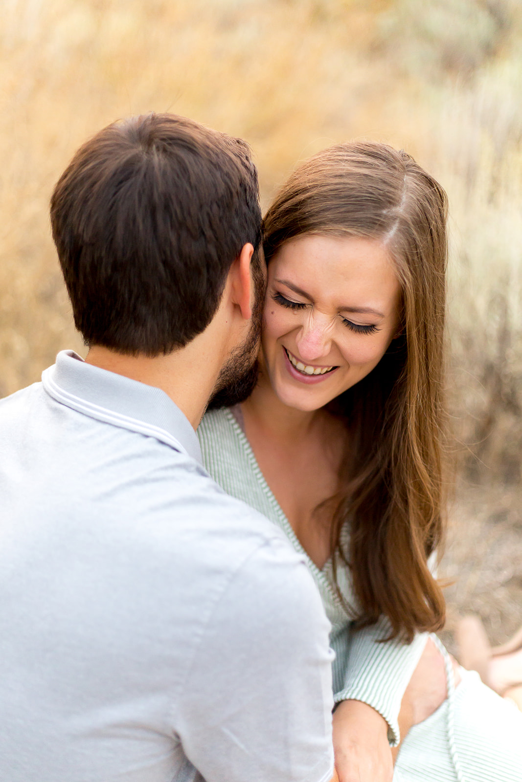 Man in a blue shirt whispers into his fiance's ear as she smiles and laughs captured by their engagement photographer