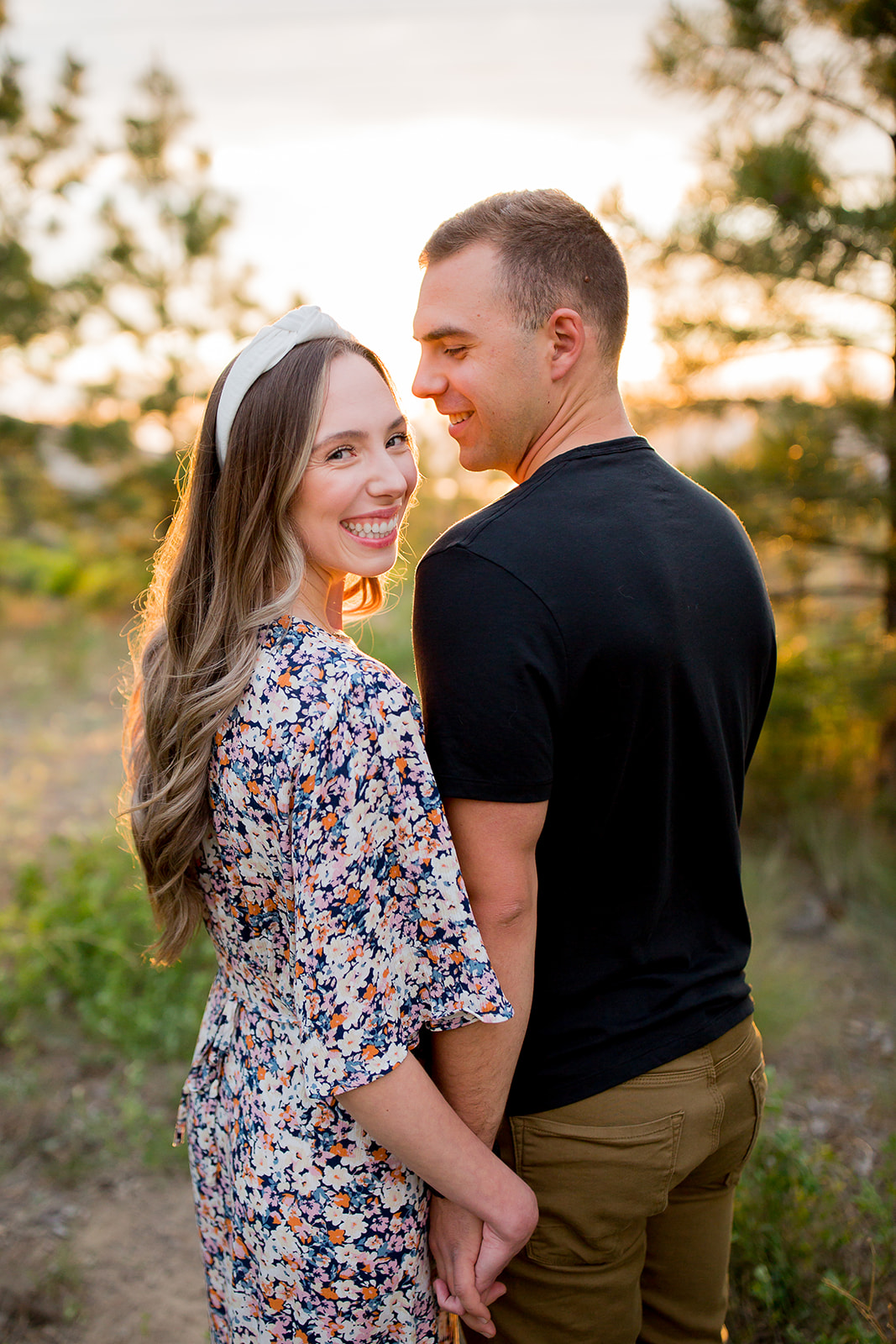 Woman smiles back at her engagement photographer while holding hands with her fiance during their outdoor photoshoot
