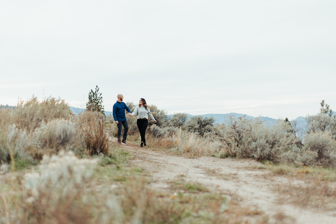 couple strolls together holding hands and smiling outside during their Okanagan engagement session 