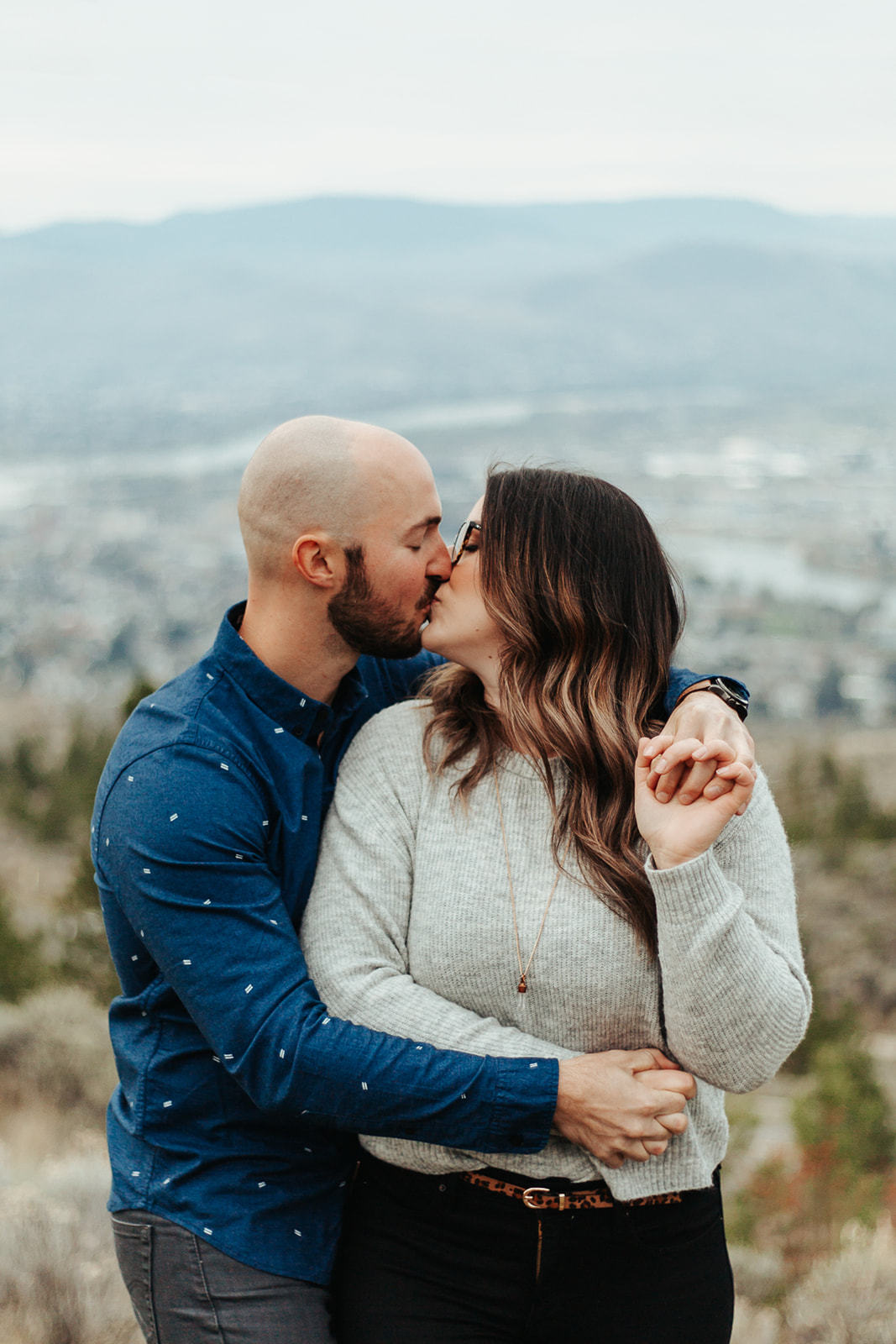 man holds his significant other and they share a kiss with the beautiful Okanagan as a backdrop
