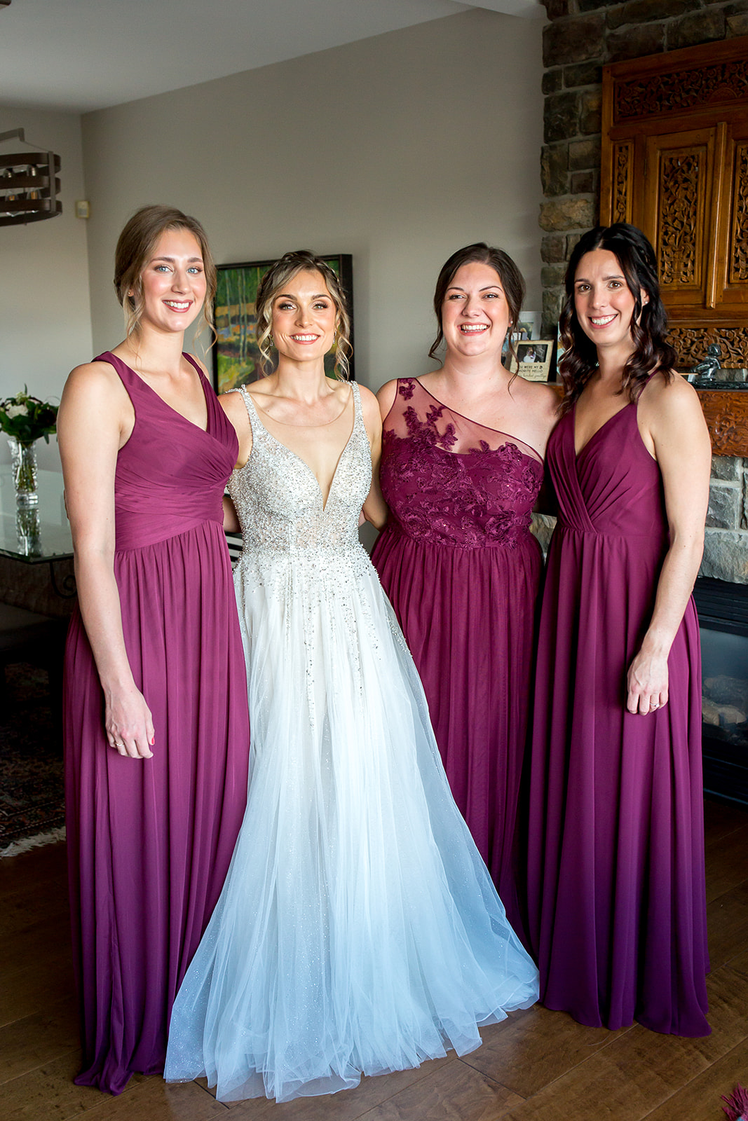 Bride stands amongst her bridesmaids wearing long, burgundy dresses as they all smile and pose before the Monte Creek Winery wedding ceremony