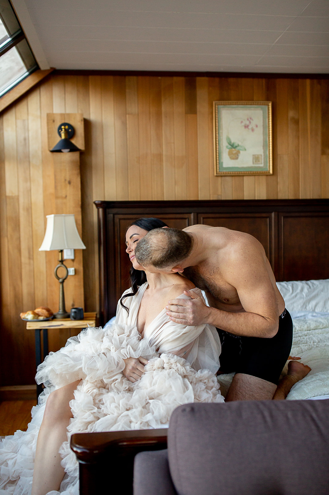 Woman wearing a gorgeous ruffled robe is kissed on the neck by her husband during their steamy vow renewal photoshoot