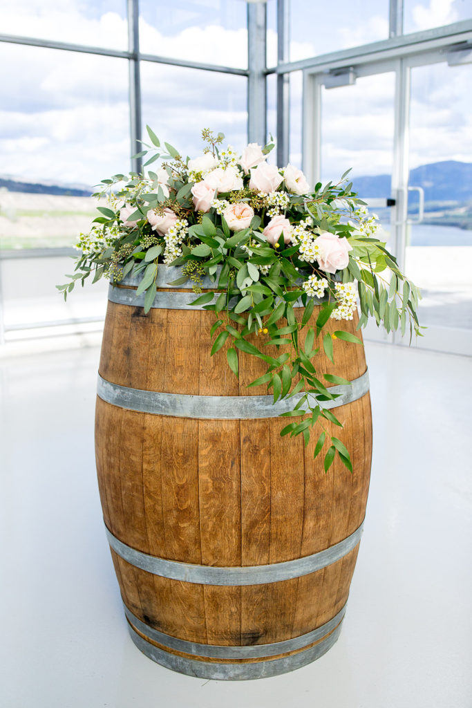 Stunning light pink florals atop a wooden barrel on display for a wedding inside a greenhouse at Monte Creek Winery in BC