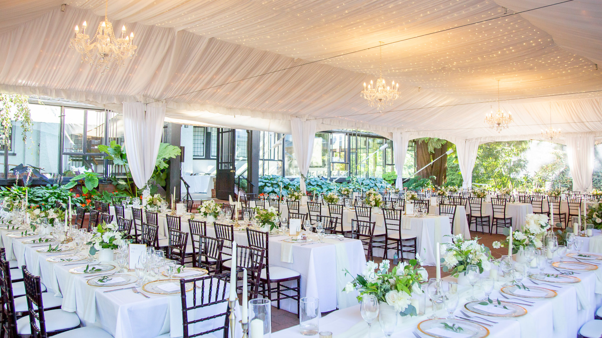 Wide angle photo of the brockhouse restaurant venue with wedding decor. White linens, brown chiffre chairs, warm toned chandeliers and greenery.